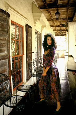 a woman in a long dress is standing on a porch next to a window .