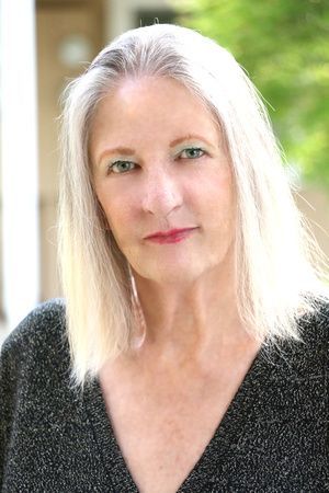 a woman with long white hair is wearing a black sweater and looking at the camera .