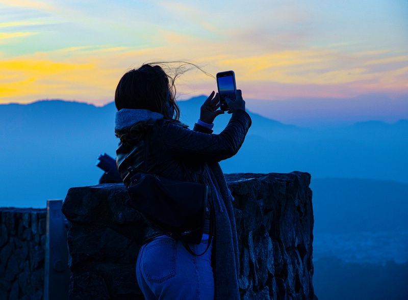a woman is taking a picture of the sunset with her cell phone .