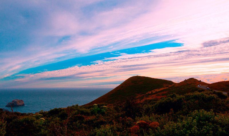 there is a sunset over the ocean with a mountain in the foreground .