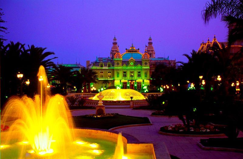 a fountain is lit up in front of a building at night