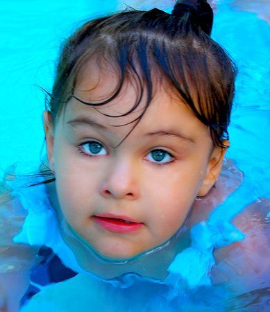 a little girl is swimming in a pool and looking at the camera .