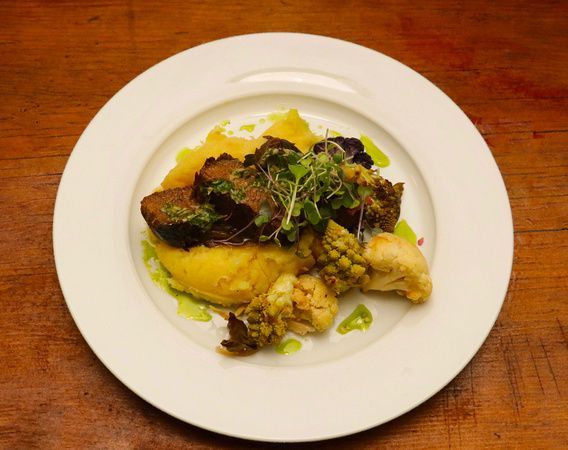 a white plate topped with meat and vegetables on a wooden table