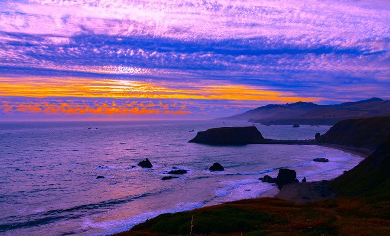 a sunset over a body of water with a cliff in the foreground .