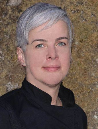 a woman with short gray hair and green eyes is wearing a black jacket .
