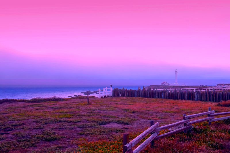 a pink and purple sunset over the ocean with a wooden fence in the foreground .