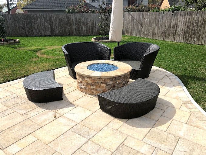 A paver patio with black plastic wicker chairs and a gel fire pit