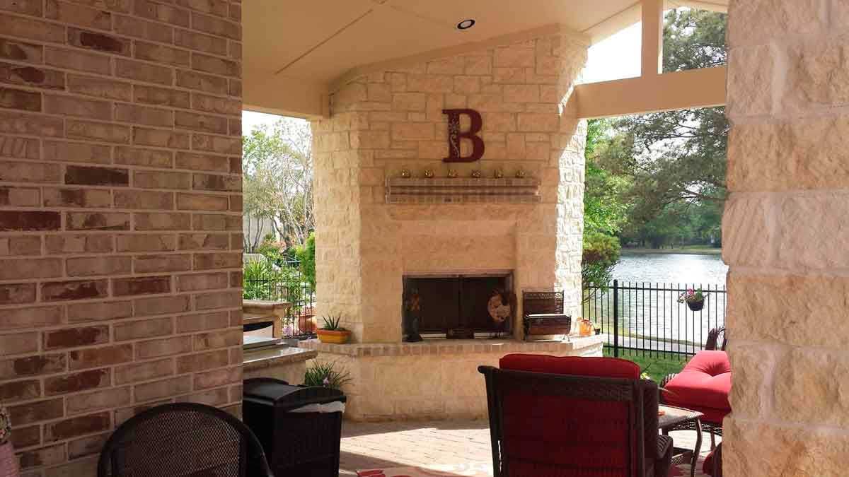 A covered patio with a stone fireplace and chairs