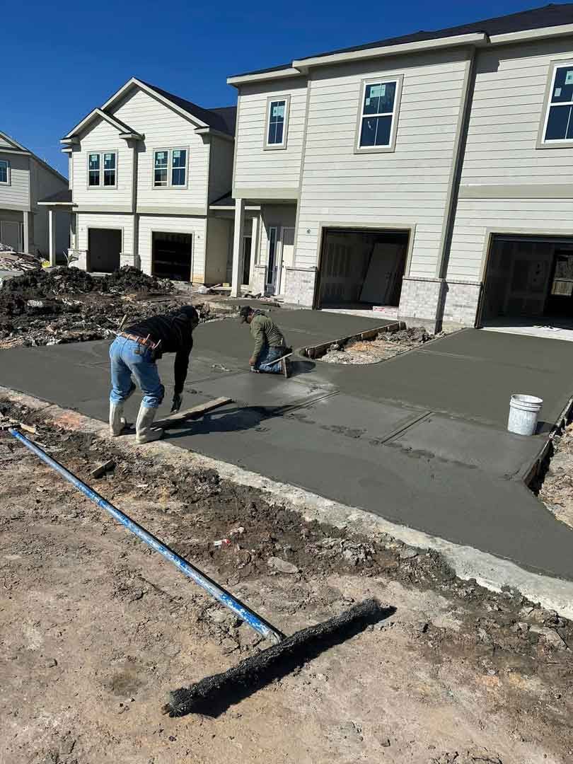 A man is spreading concrete on a sidewalk in front of a house.