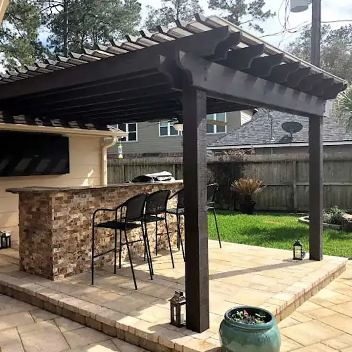 There is a pergola over a patio with a bar and chairs.