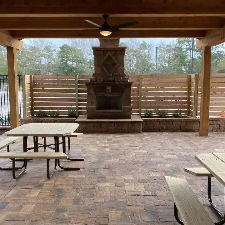 A patio with a fireplace and picnic tables under a pergola.