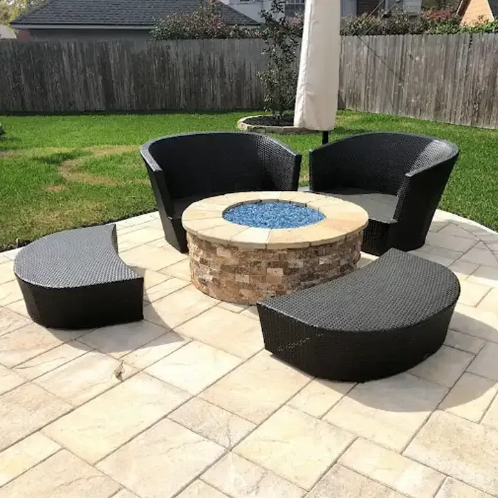 A fire pit is surrounded by wicker furniture on a patio.