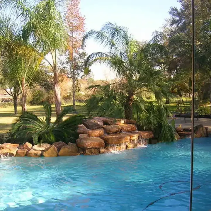 A swimming pool with a waterfall and palm trees in the background