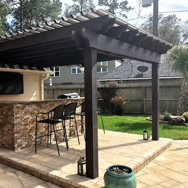 There is a pergola over a patio with a bar and chairs.