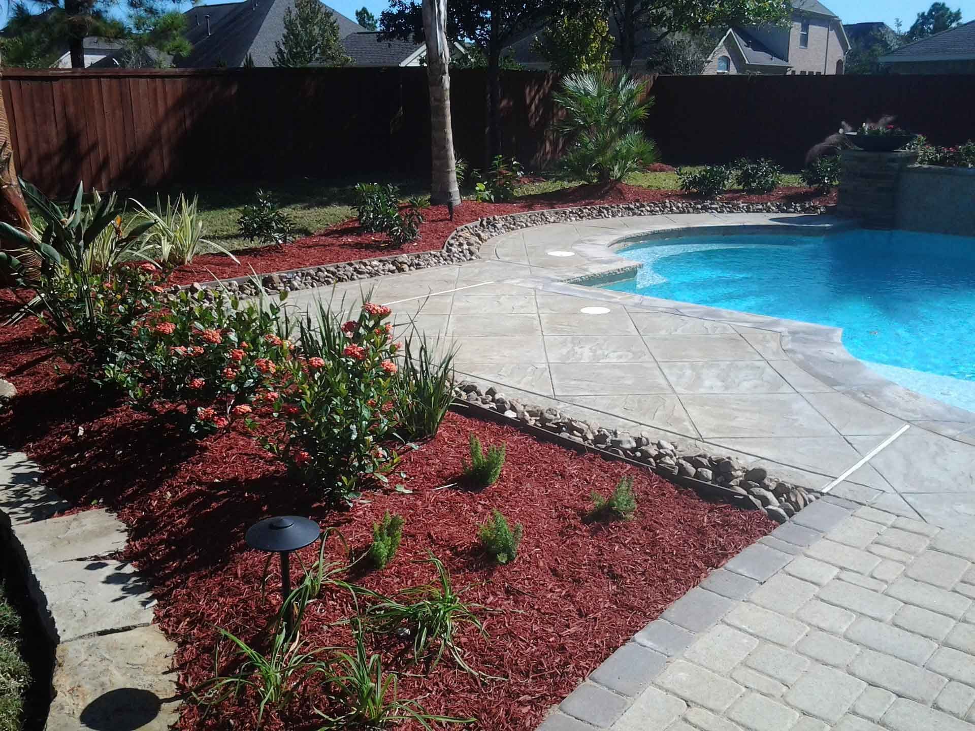 A swimming pool is surrounded by red mulch and flowers.