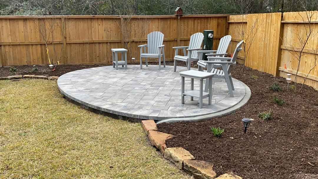 A small circular patio made of gray bricks with chairs and landscaping