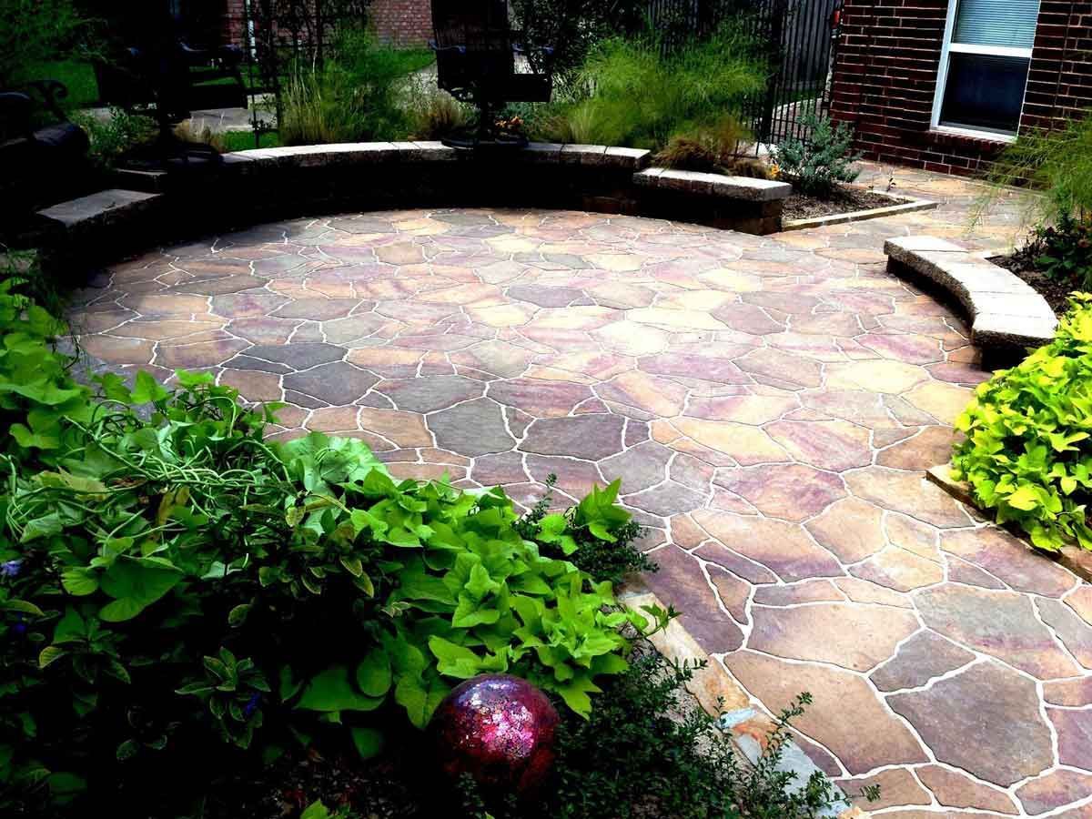 A beautiful circular patio of light stones and landscaping bed