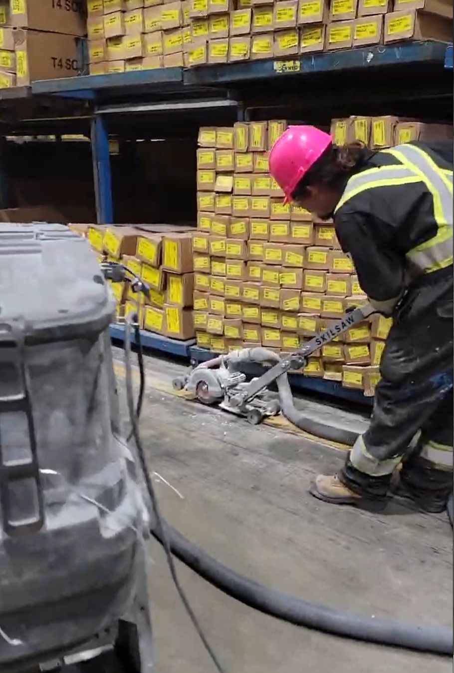 Person in pink hard hat using a concrete saw with dust collection, in a warehouse setting.