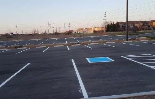 Empty asphalt parking lot with white painted lines and a blue accessible parking space.