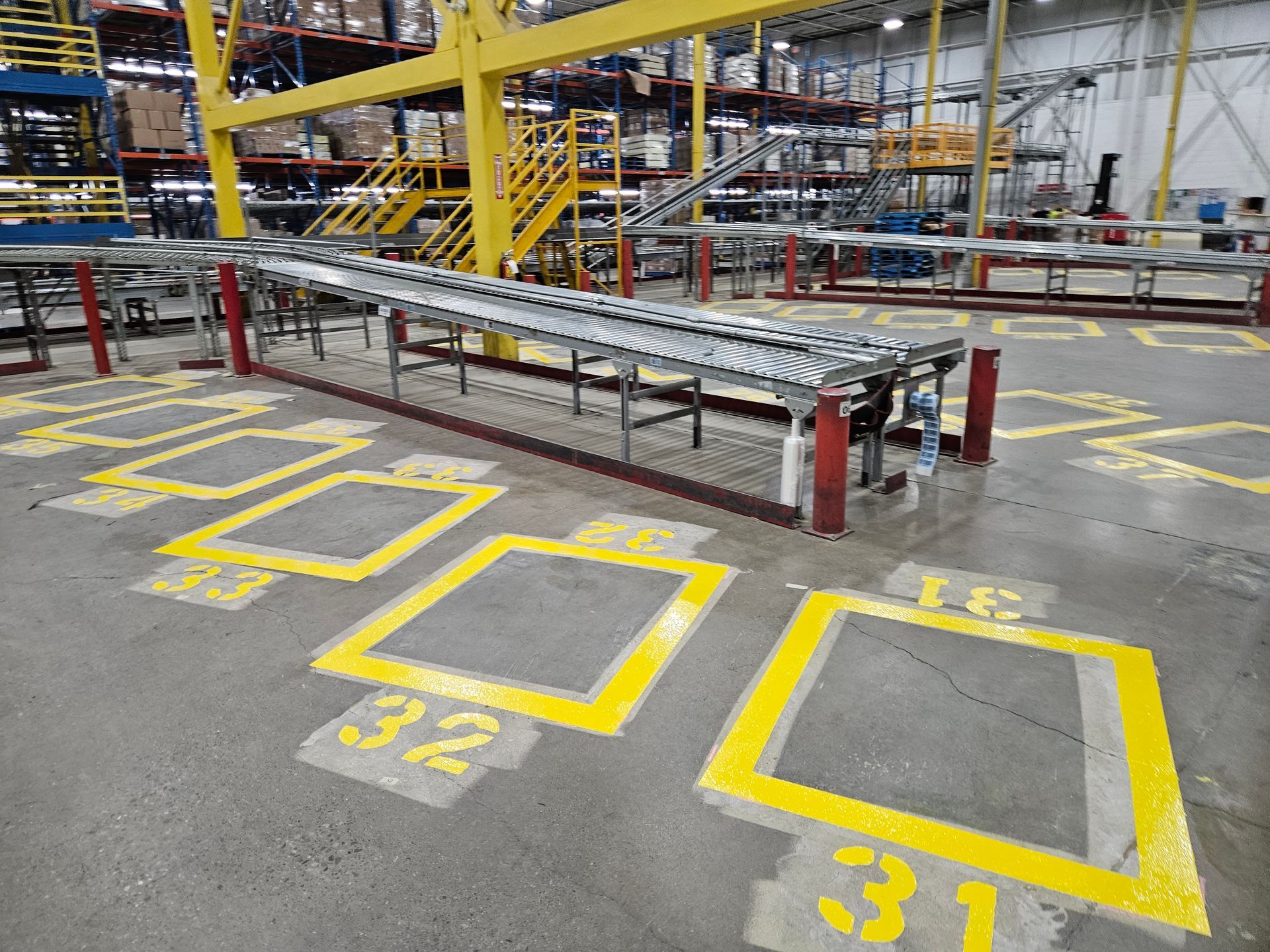 Warehouse interior with conveyor belts and numbered yellow floor markings.