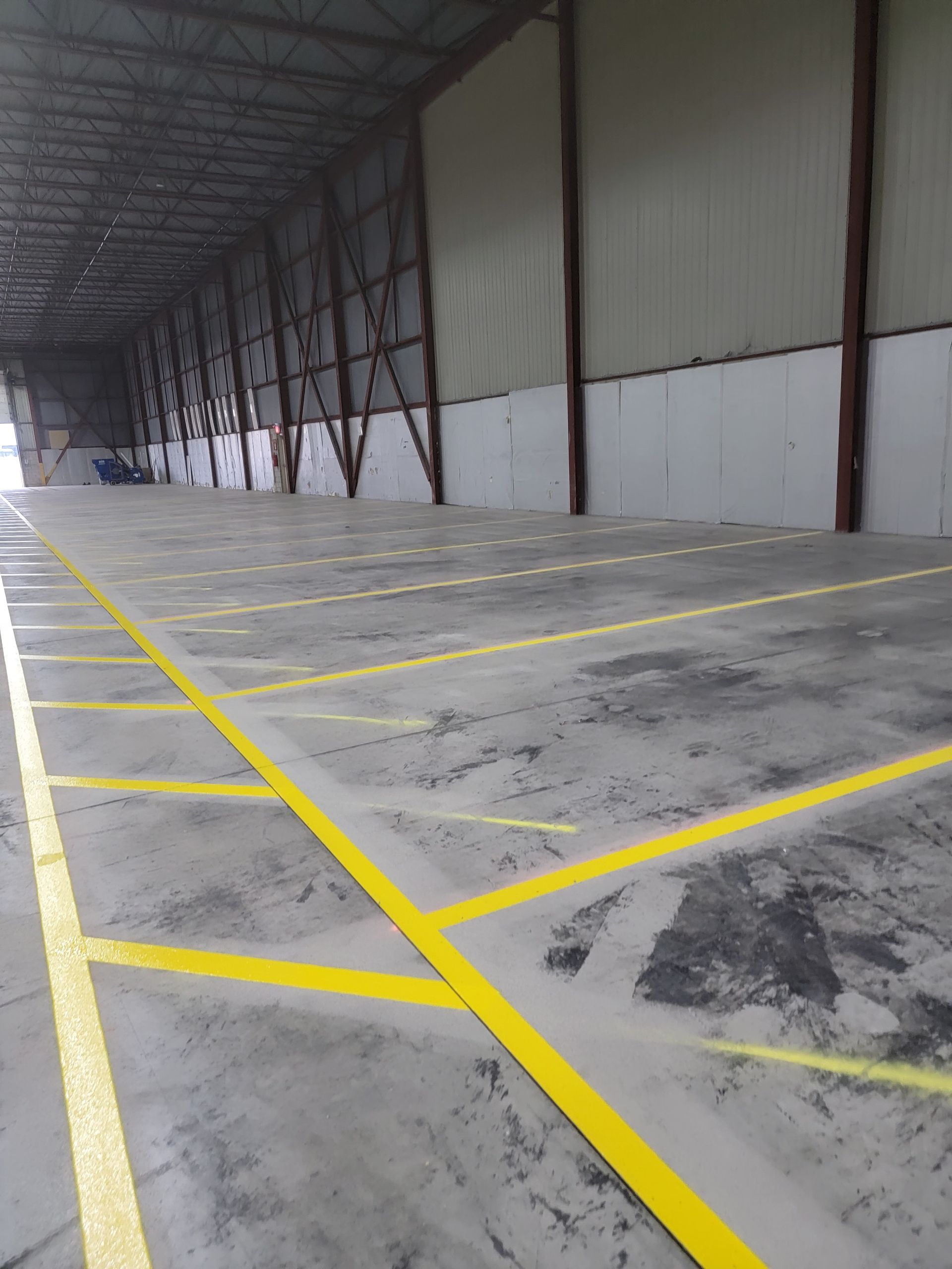 Interior view of a large warehouse with yellow painted lines on the concrete floor; metal structure visible.