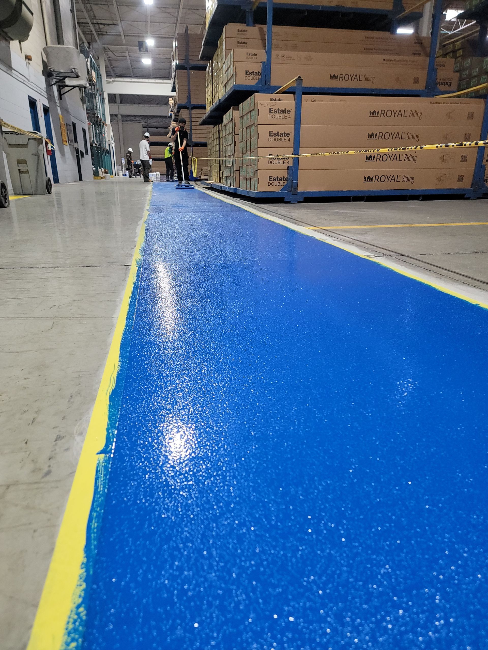 Blue painted walkway in a warehouse, a person walks down the aisle, stacked boxes on the right.