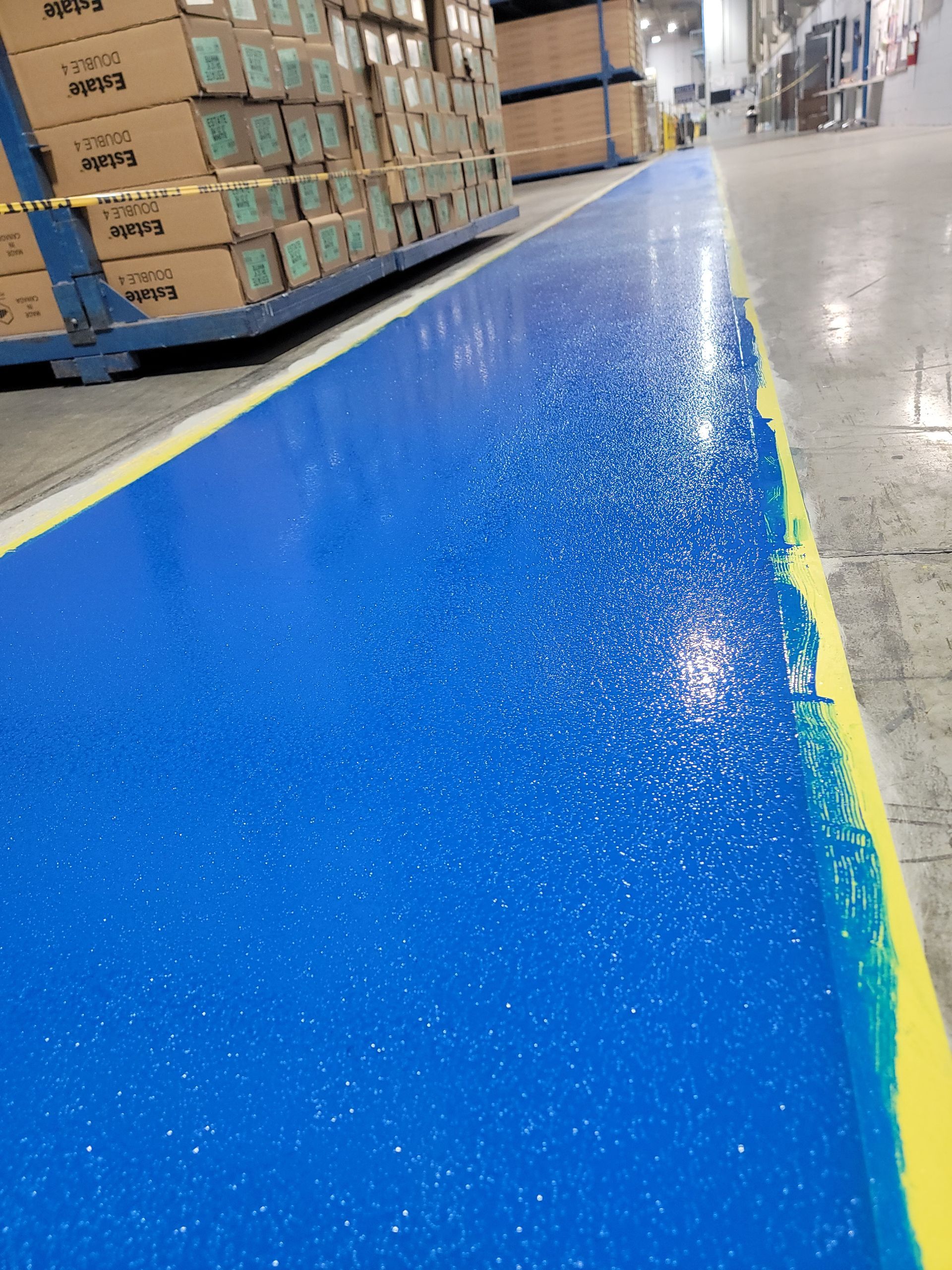 Blue painted floor in warehouse, with yellow and white border, and boxes in background.