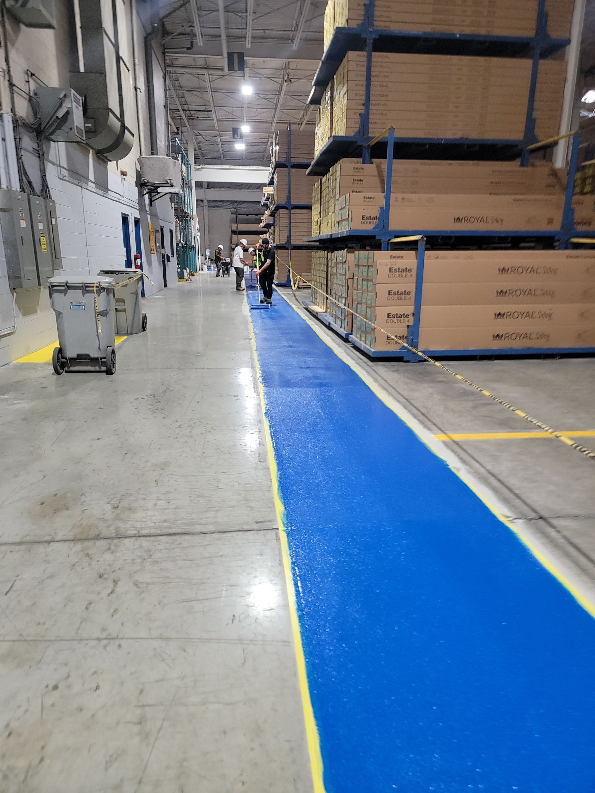 Warehouse with a blue painted aisle, workers, and stacks of boxes.