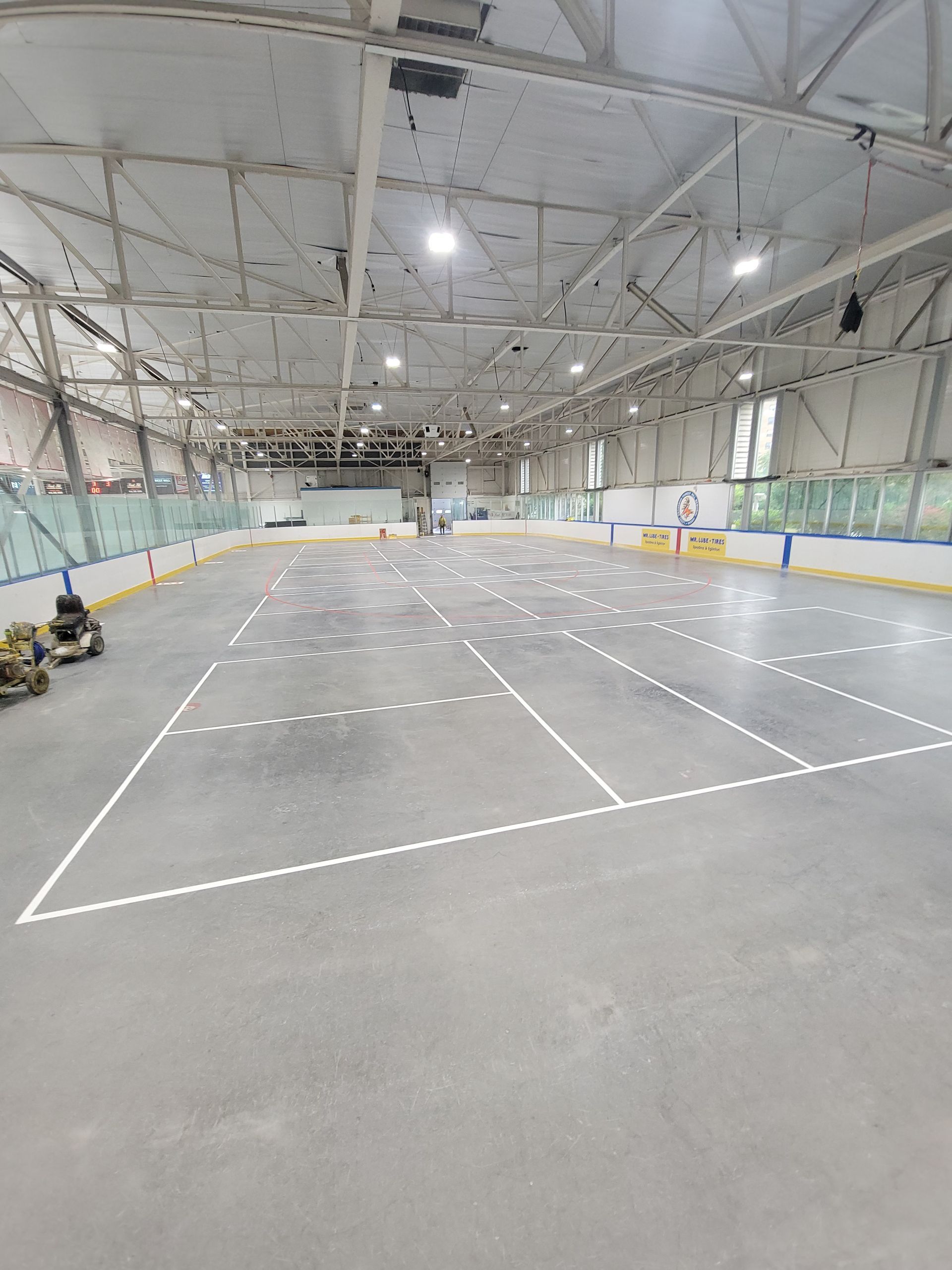 Empty indoor hockey rink with white lines on gray surface, overhead lighting.