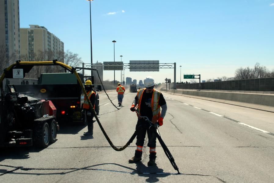 Highway workers repairing road cracks with equipment on a sunny day.