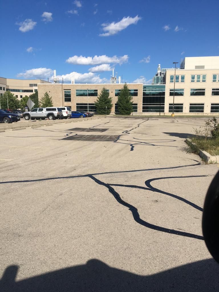 Parking lot in front of a modern building with a blue sky. Several cars and trees are visible.