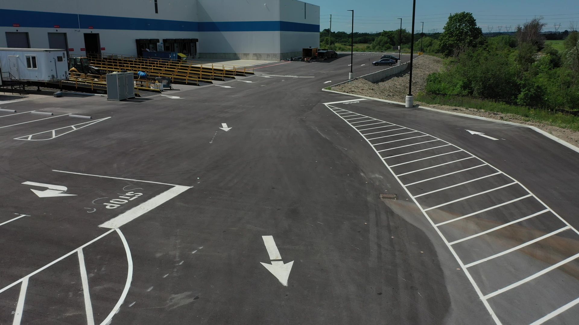 Asphalt parking lot with white painted directional arrows and parking space lines, next to a large blue and white building.
