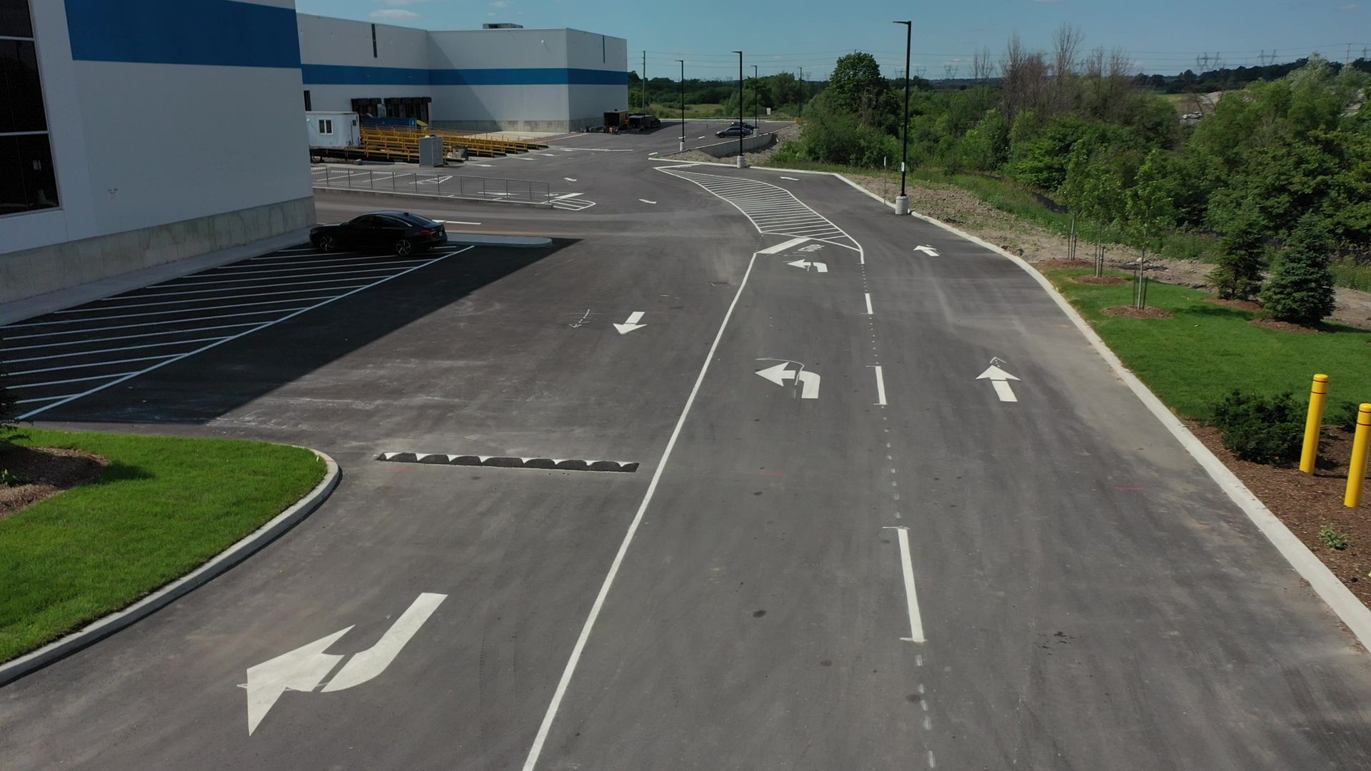 Asphalt road with directional arrows, next to a building and greenery.