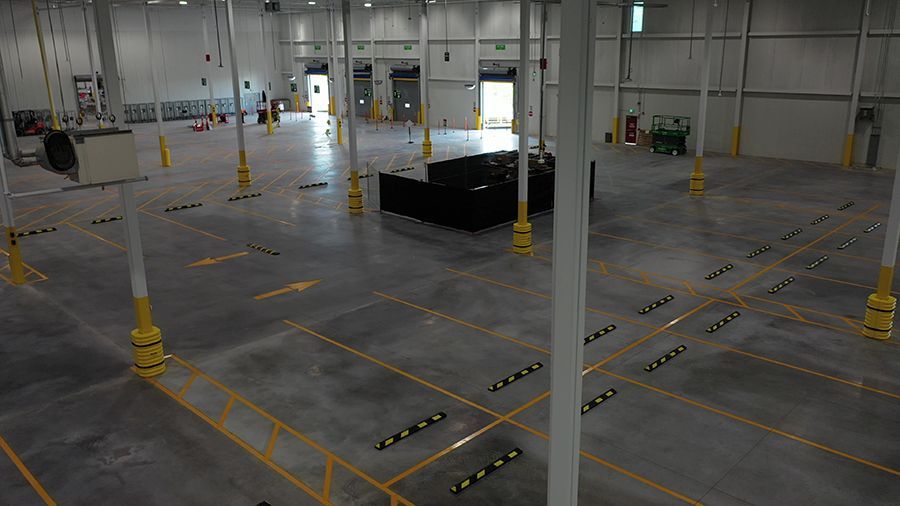 Large, empty warehouse interior. Concrete floor, numerous pillars, yellow safety markings, overhead lighting, loading docks.
