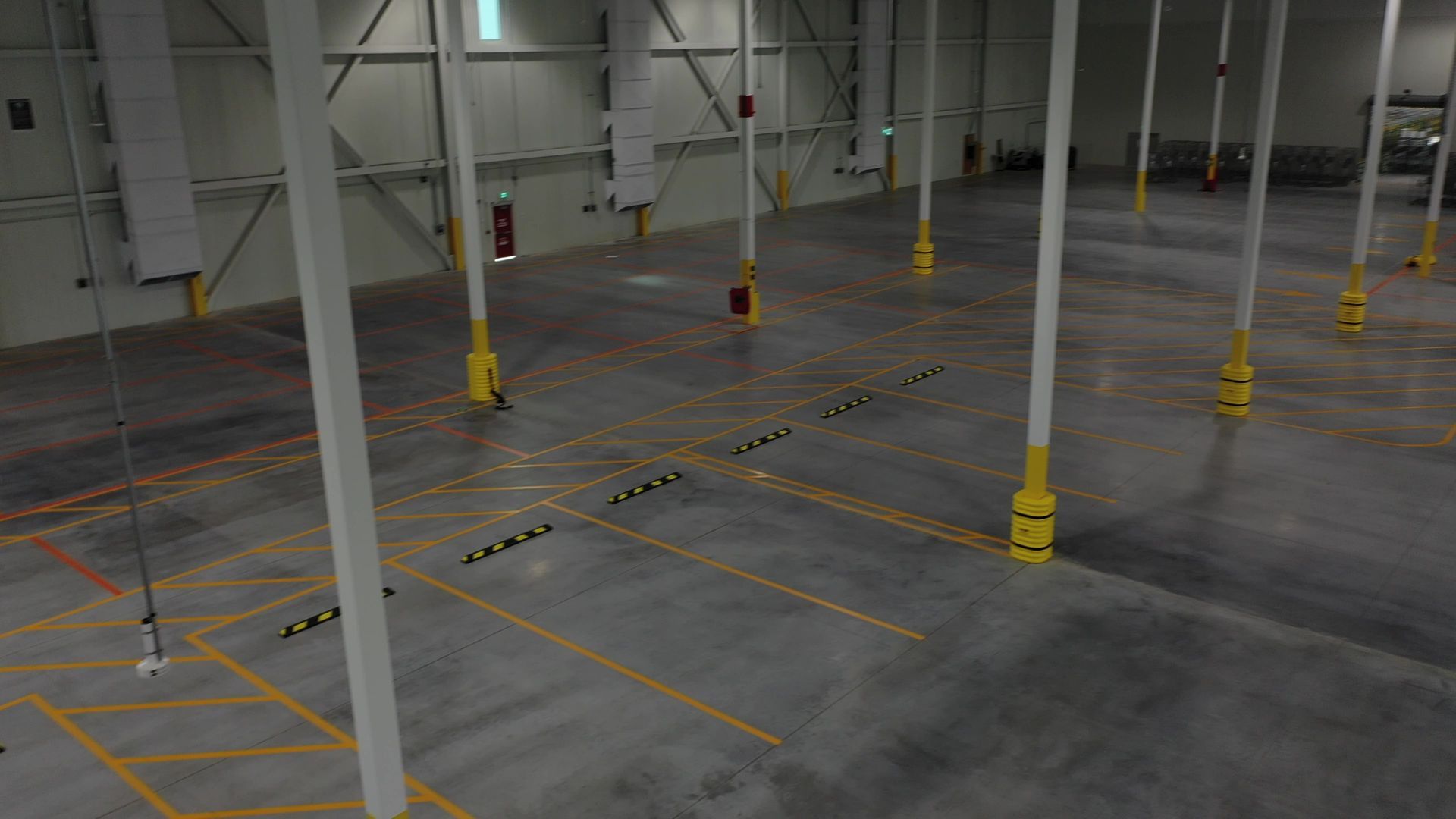 Empty warehouse with concrete floor, yellow safety markings, and support columns.
