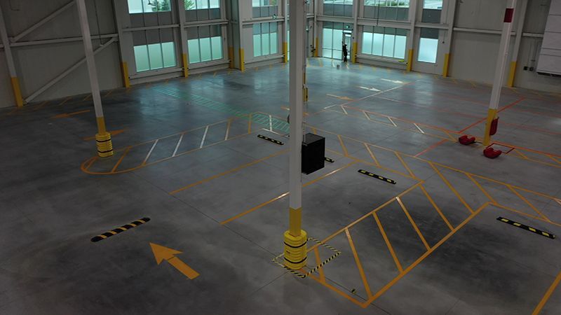 Warehouse interior with yellow markings on the floor, pillars, and a person in the distance.
