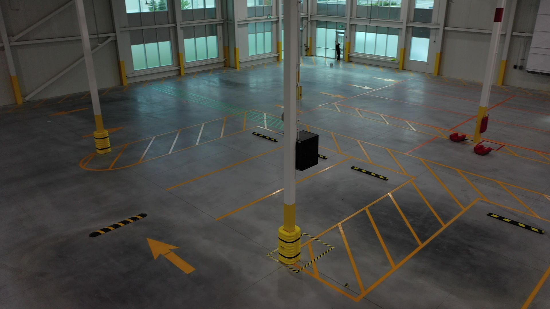 Empty industrial warehouse interior with concrete floor, yellow markings, and a lone person.