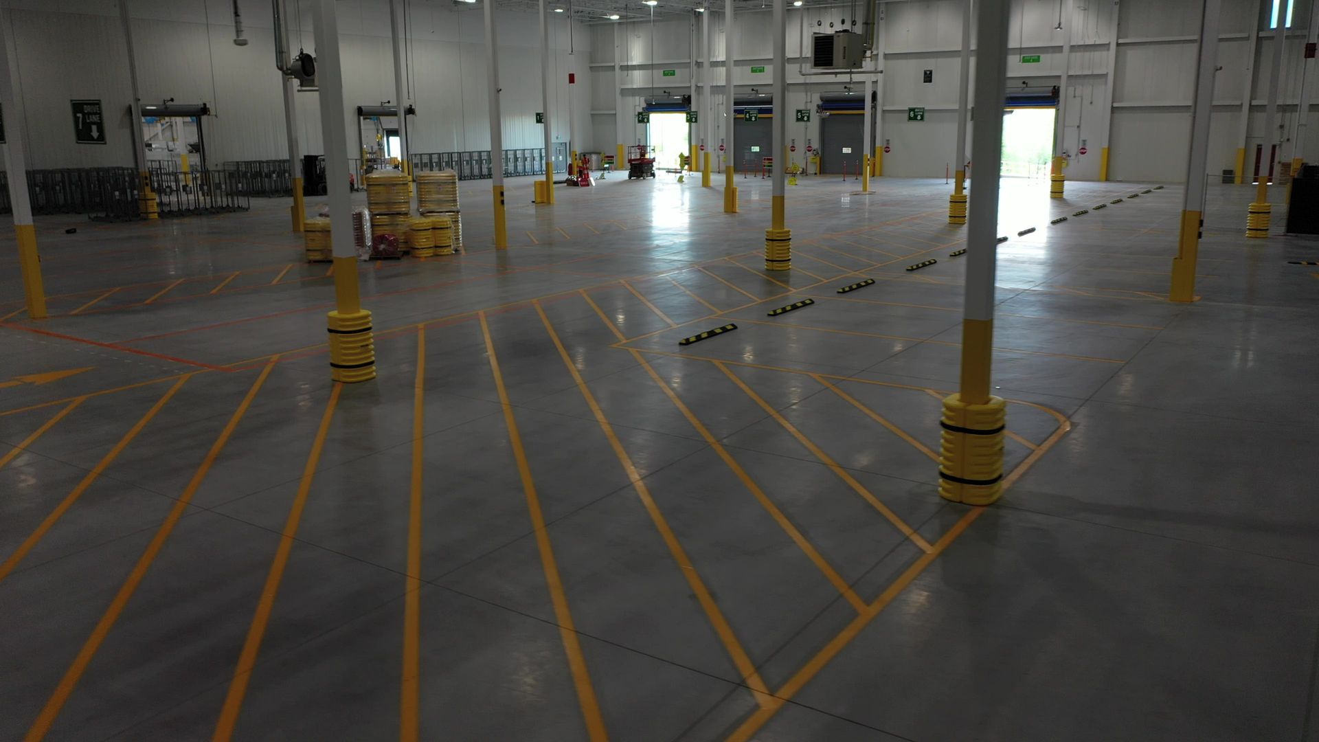 Empty warehouse interior with yellow painted pillars, lines on the floor, and open doors.