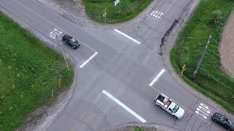Aerial view of a four-way intersection with crosswalk markings; two vehicles are present.