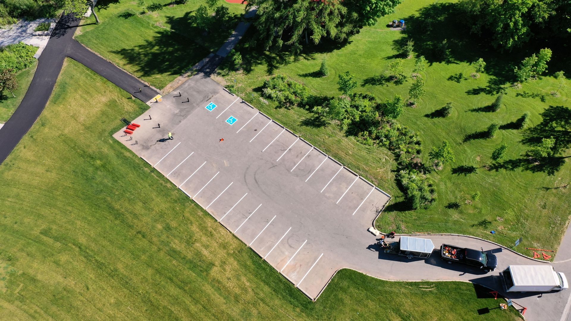 Overhead view of an empty parking lot surrounded by green grass and trees.