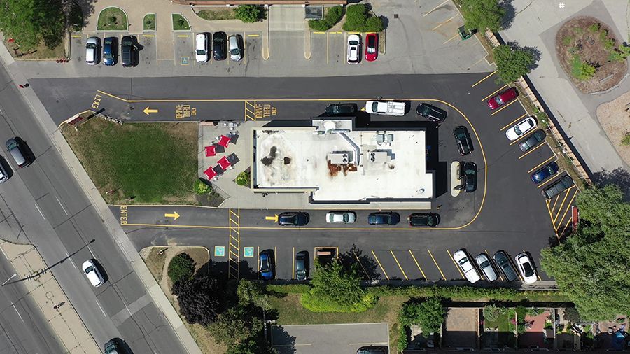 Aerial view of a restaurant with drive-thru, parking, cars, and landscaping, set on a city street.
