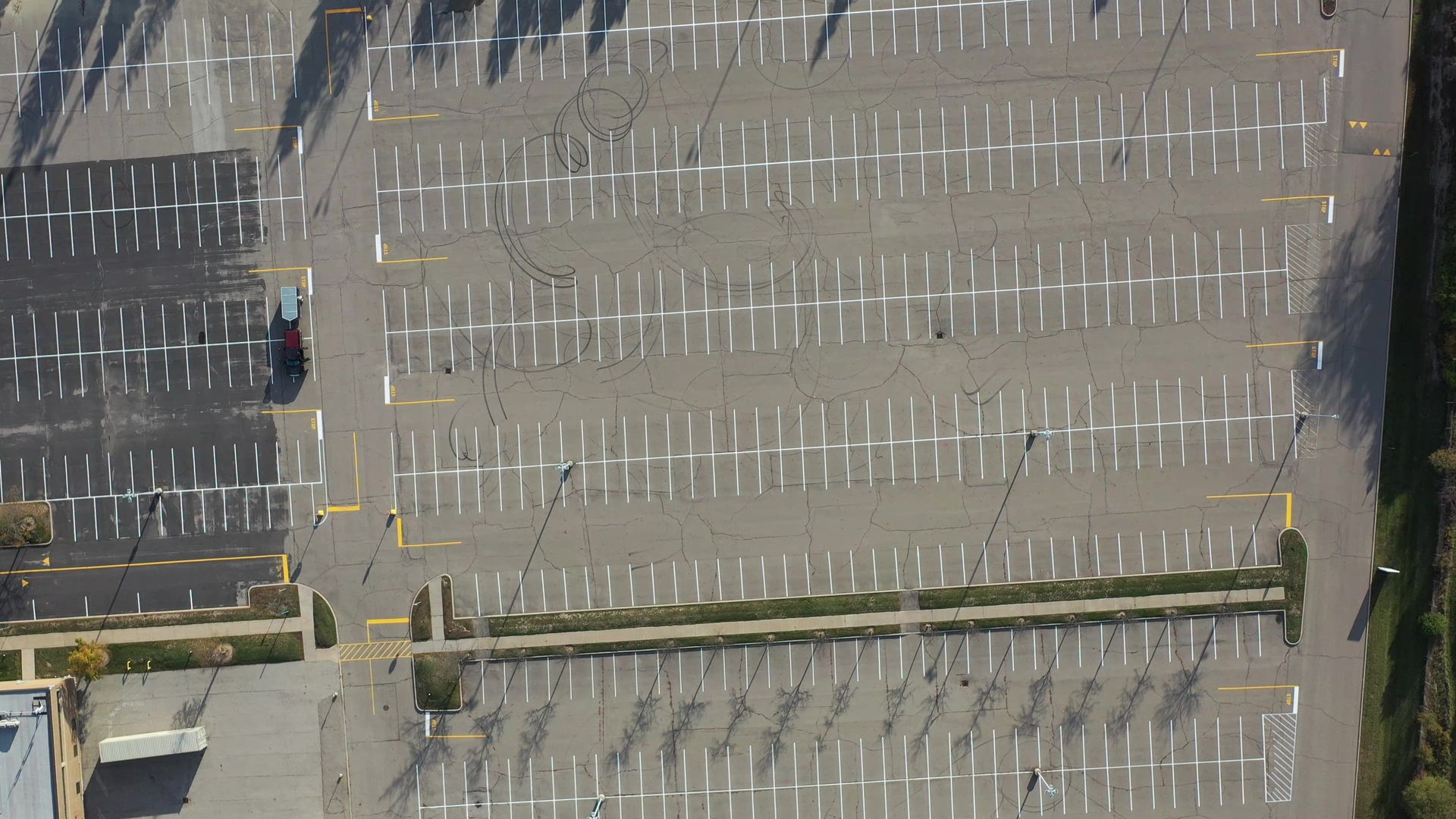 Overhead view of a mostly empty parking lot with white parking space markings; a red car is driving in the lot.