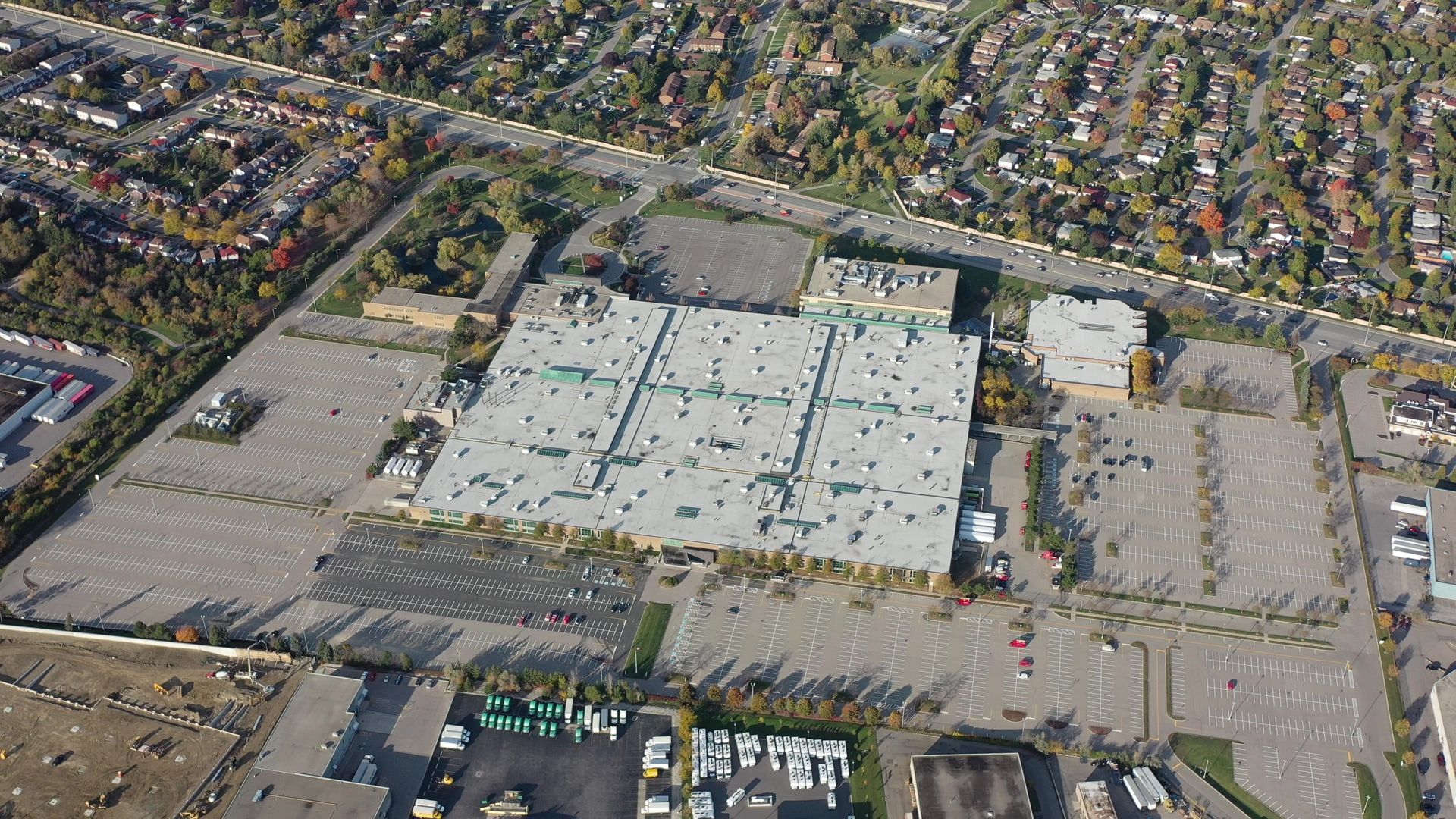 Aerial view of large commercial building surrounded by vast parking lots, near residential area with autumn trees.
