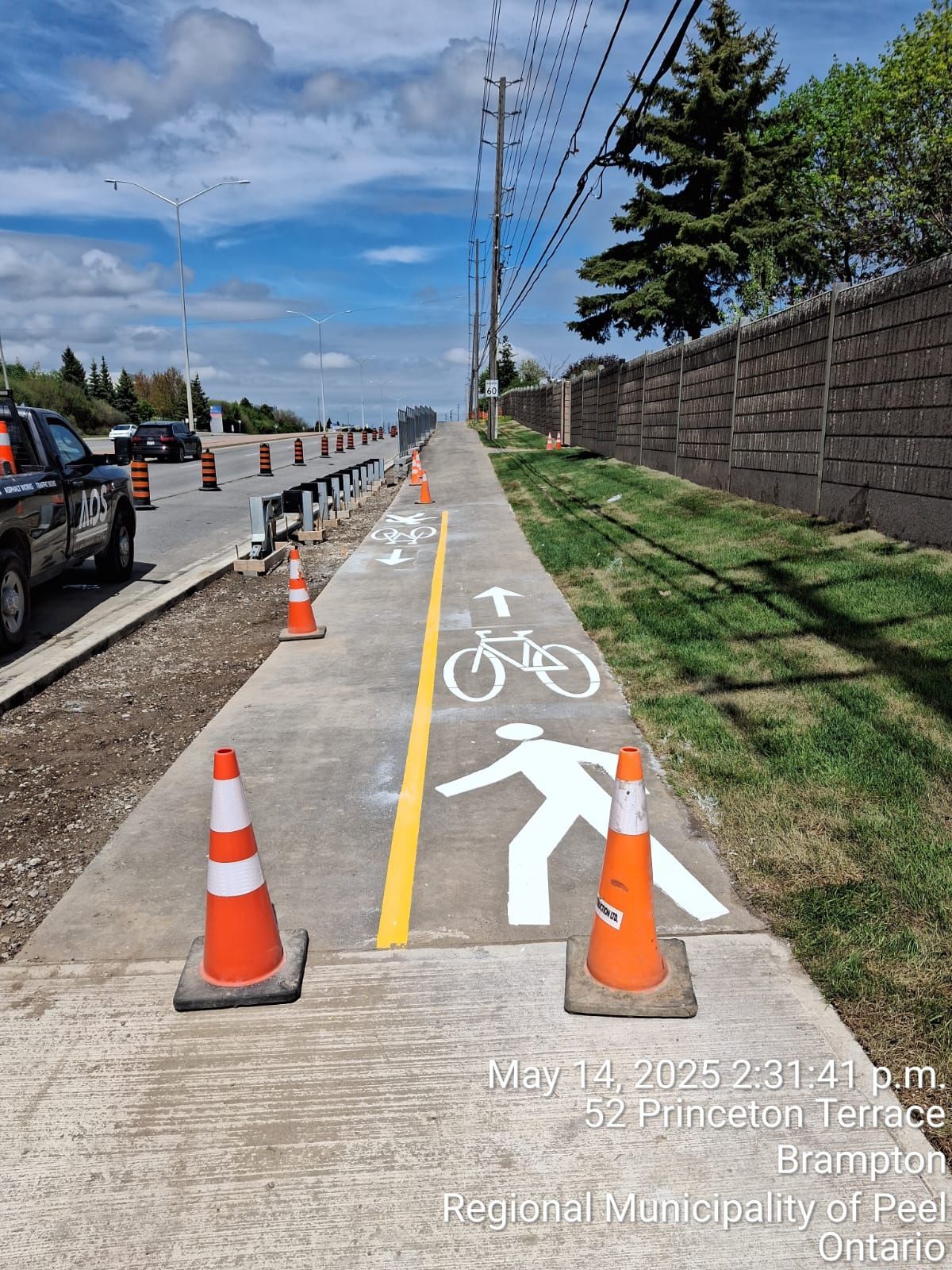 New multi-use path with pedestrian and bike symbols, construction cones, and a concrete barrier.