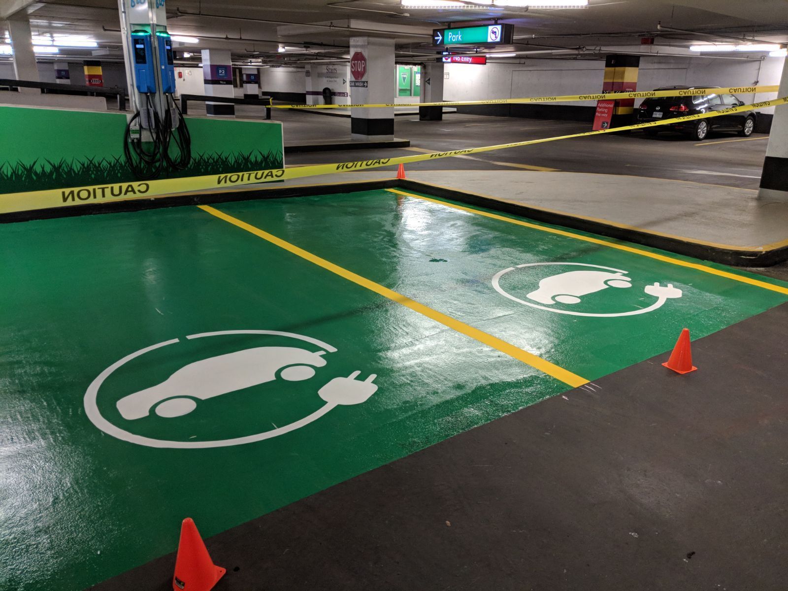 Electric vehicle charging station in a parking garage. Green painted surface with car symbols. Yellow tape surrounds the area.