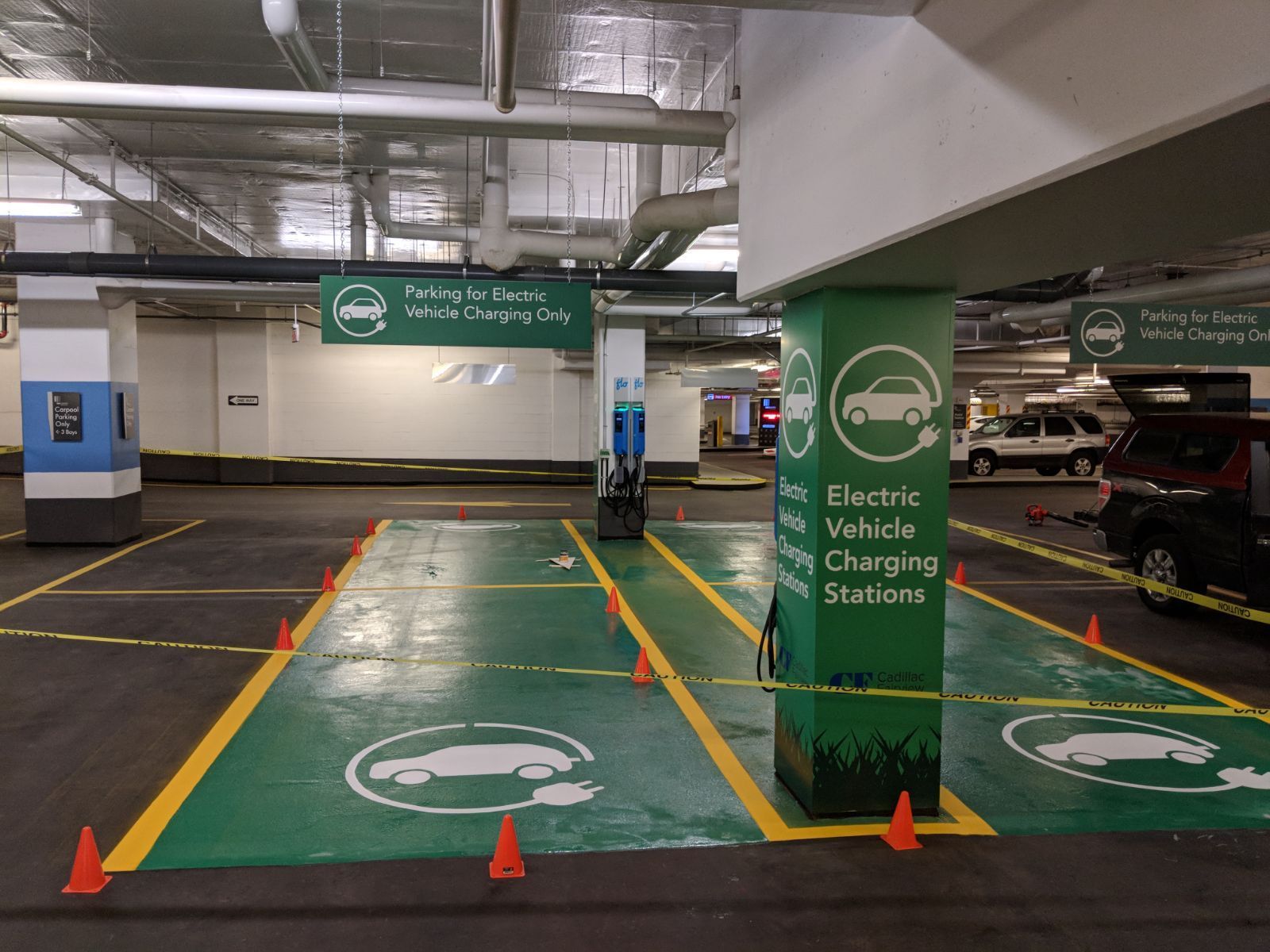 Underground parking garage with electric vehicle charging stations, painted green with orange cones.