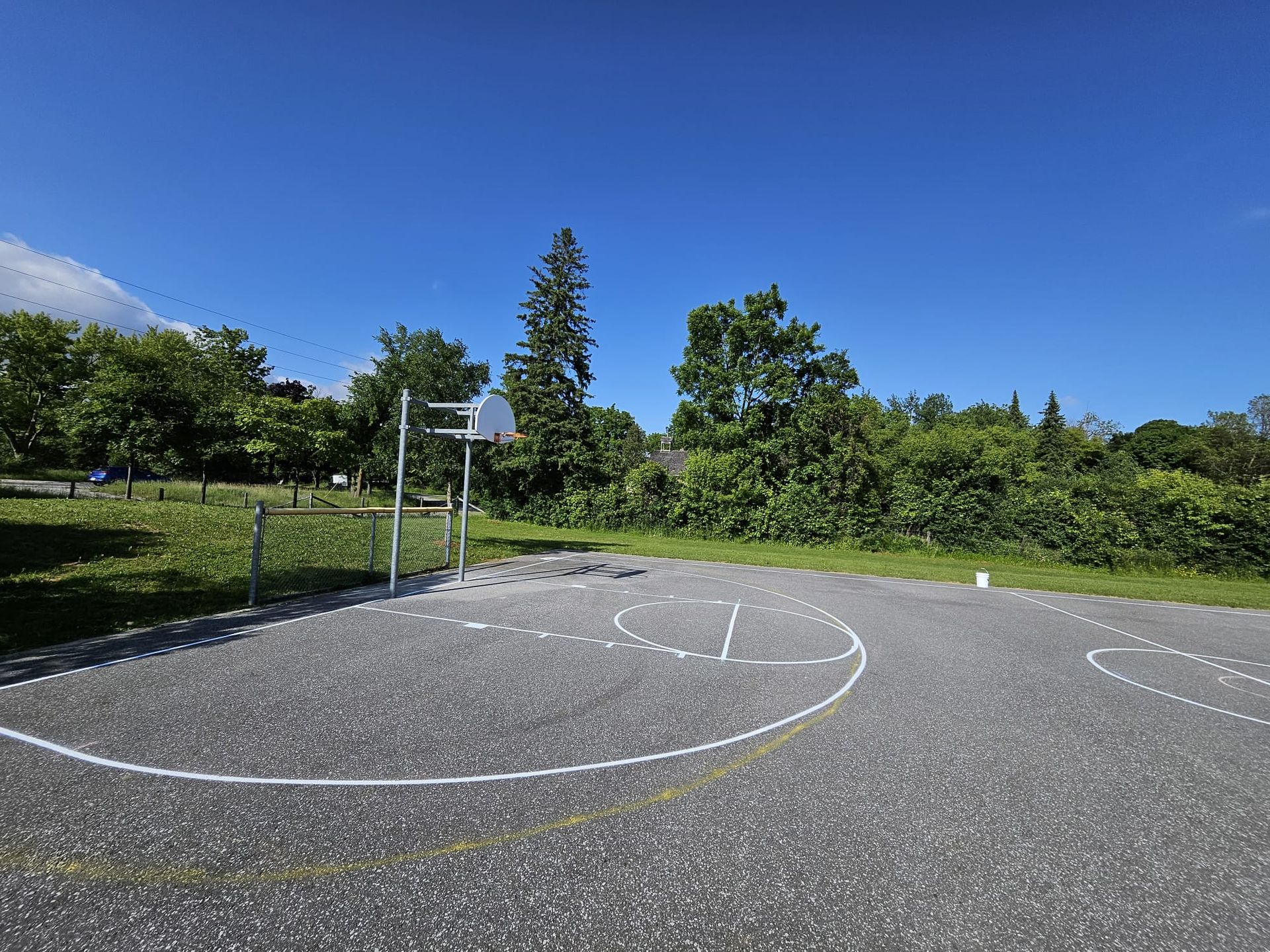 Basketball court under a blue sky, surrounded by grass and trees.