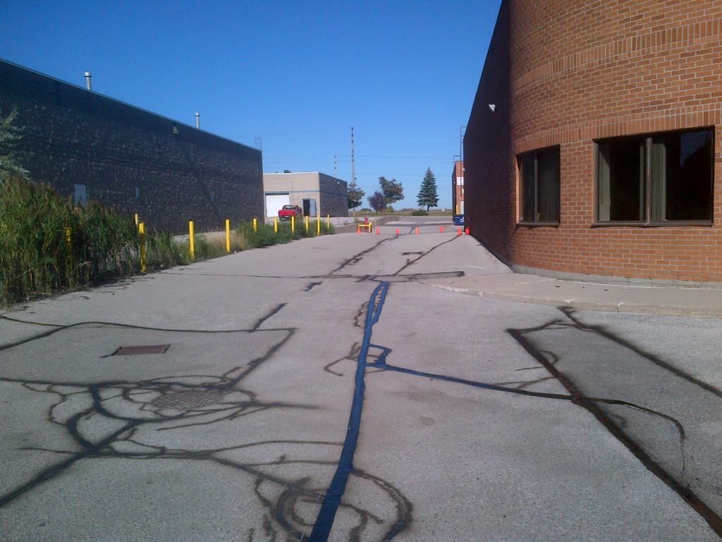 Asphalt road with cracks, flanked by brick building and industrial structures, under a clear blue sky.