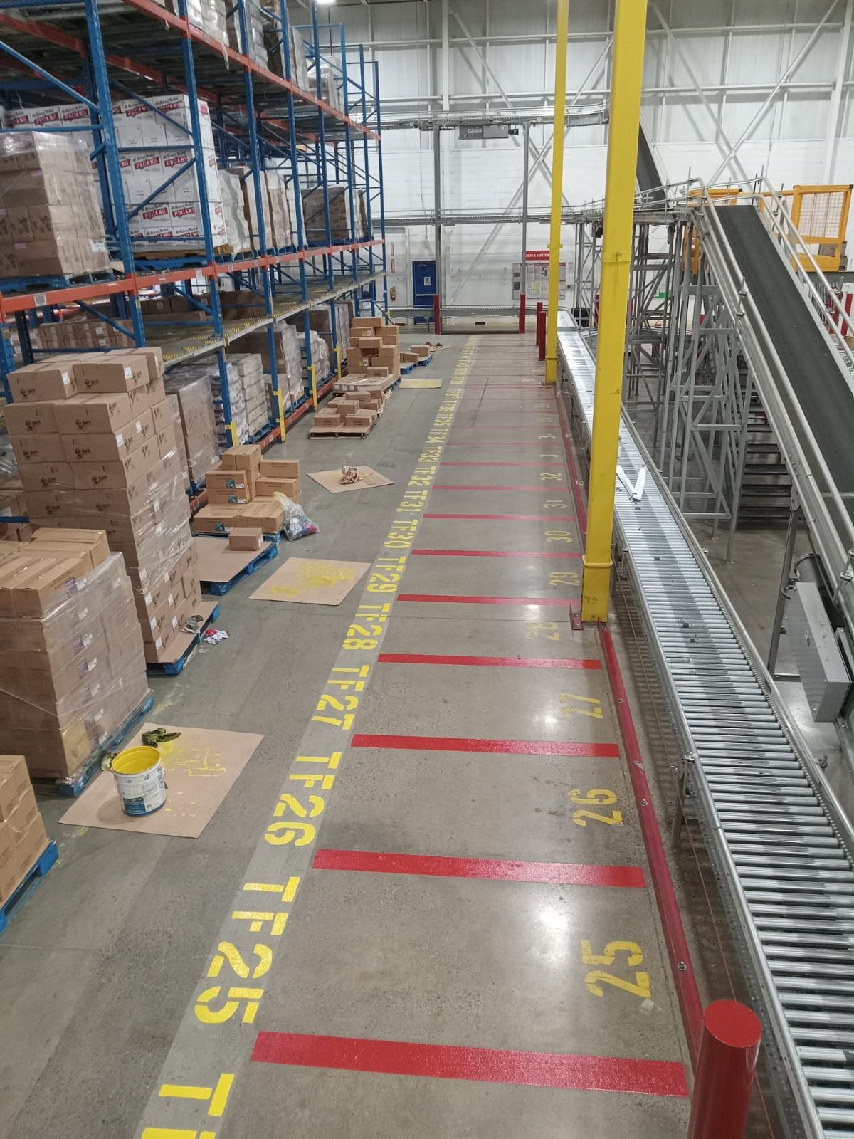 Warehouse interior with pallets, shelving, and conveyor belt, featuring floor markings for truck bays.