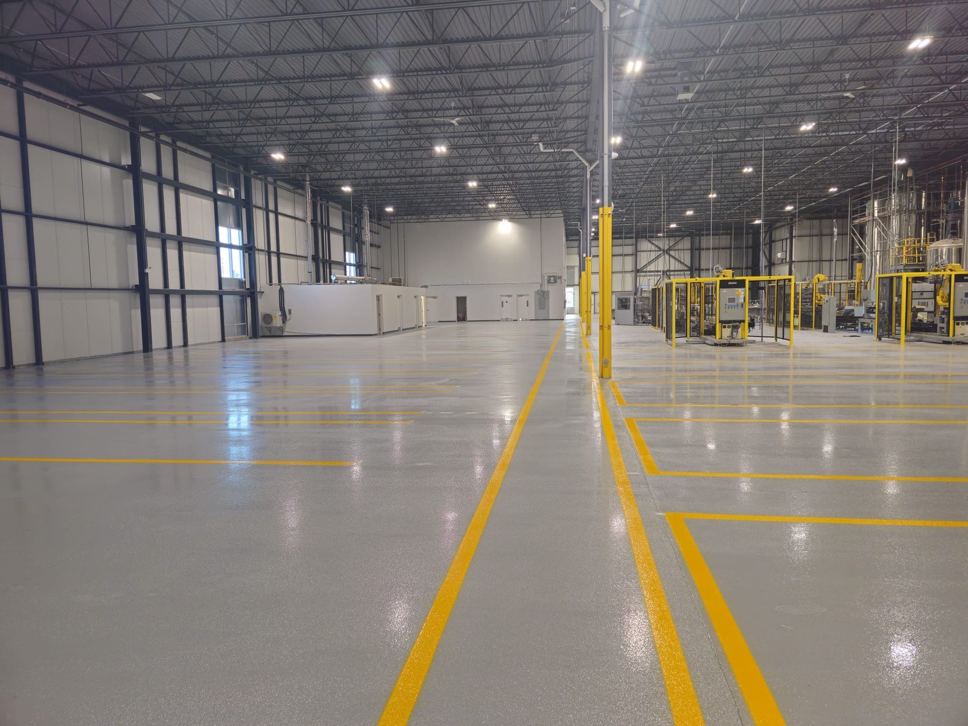Large, empty factory interior with gray floor, yellow lines, and equipment.